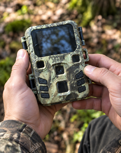 Chasseur tenant la caméra Hunter Mini Pro à deux mains devant le sous bois pour régler les paramètres